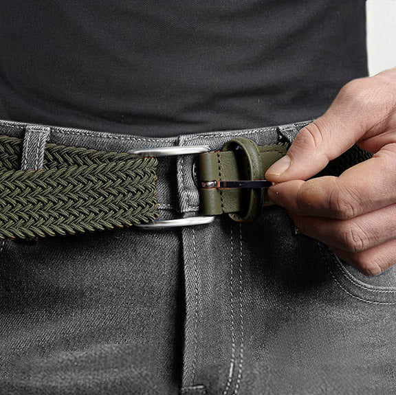 Man wearing a dark green elastic belt with silver buckle, paired with grey jeans and a black shirt