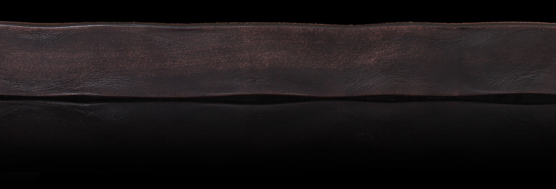 Brown solid hide leather on a black background showcasing authentic patina