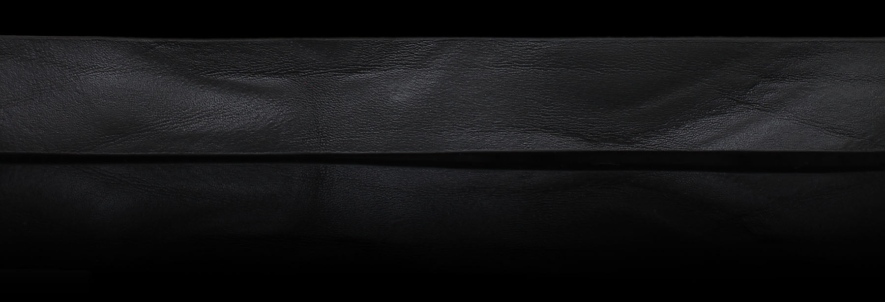 Black solid hide leather on a black background showcasing authentic patina