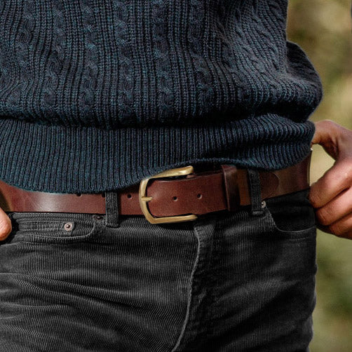 Man wearing a brown solid hide leather belt with gold brass buckle, paired with corduroy trousers and a knitted jersey