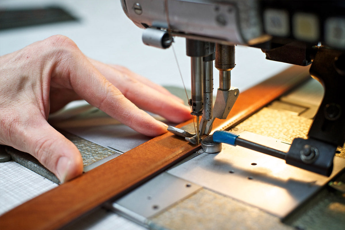 Close-up of Italian artisan stitching a leather belt on a sewing machine, reflecting traditional craftsmanship.
