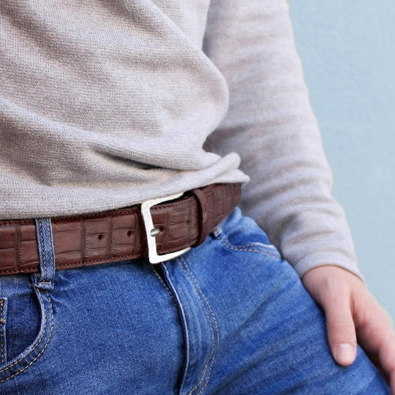 Men wearing brown crocodile leather Italian leather belt with silver buckle and blue jeans and grey sweater.